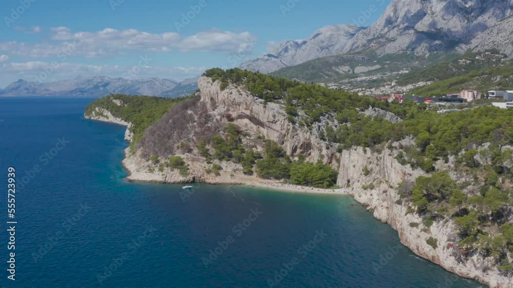 Drone video. Blue sea. Rocky coastline covered with green forests. High mountains in the distance. Blue sky, clouds. A small boat floats along the shore. Summer, sunny day. Drone video. Blue sea. Rocky coastline covered with green forests. High mountains in the distance. Blue sky, clouds. A small boat floats along the shore. Summer, sunny day.