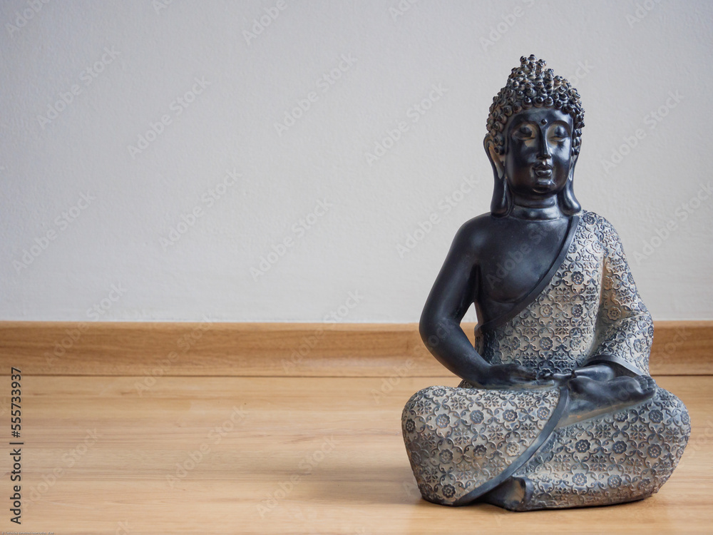Estatua de Buda sentado en el piso de madera laminada con fondo de pared gris claro, vista cerca