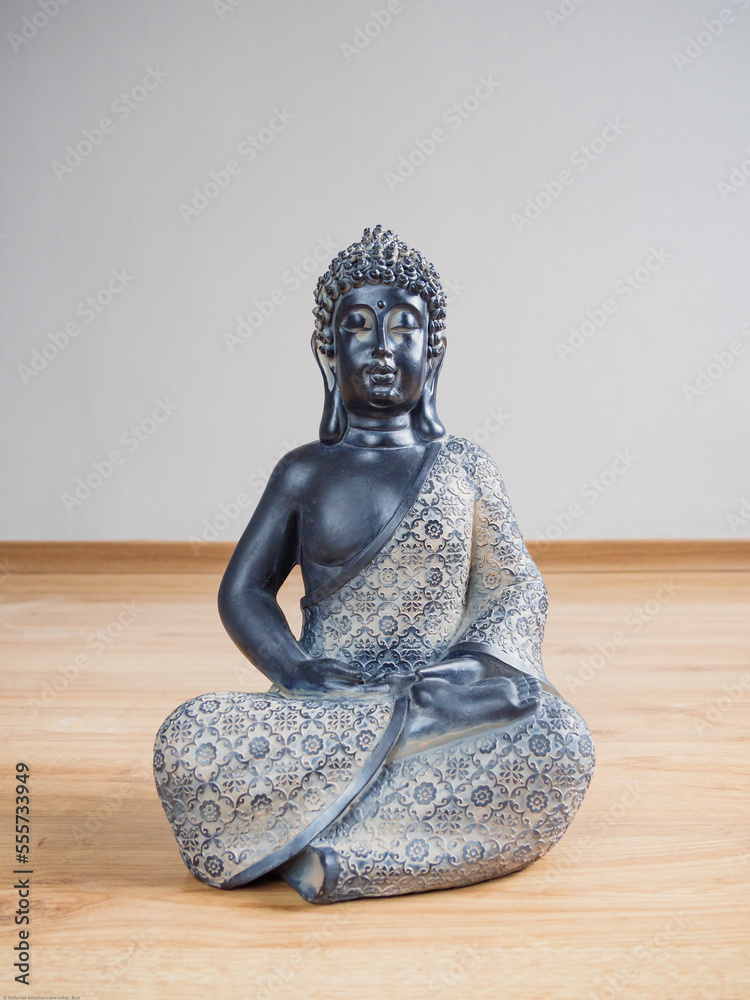 Estatua de Buda sentado en el piso de madera laminada con fondo de pared gris claro, close up.