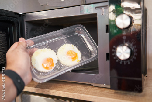 Unrecognizable person putting ready to eat fried eggs inside microwave. Supermarket fast food concept