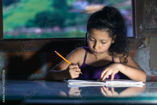 latina girl, brunette studying. little girl with a yellow pencil doing her homework, leaning on a glass table.