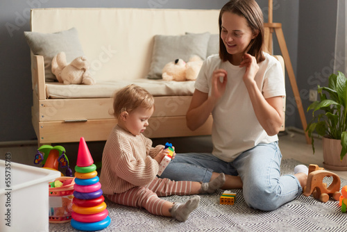 Mom and daughter playing together at a group lesson in the Montessori center, mommy and baby in casual clothes sitting on floor on carpet playing with colorful blocks.