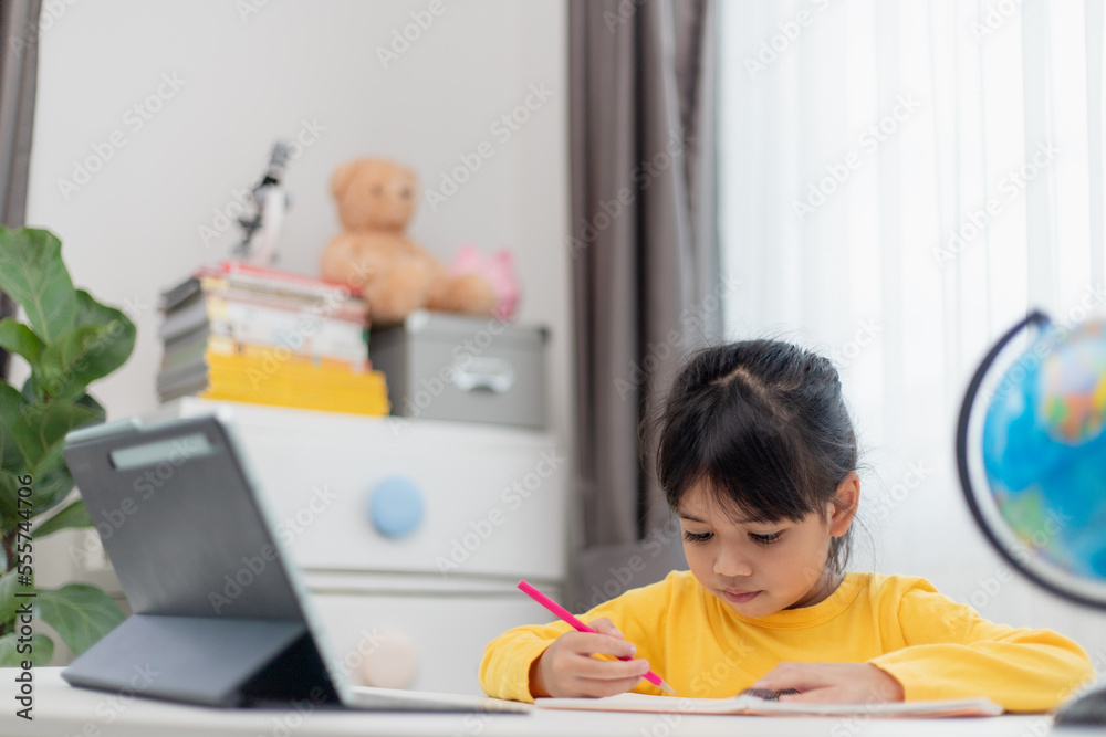 Asian schoolgirl doing her homework with digital tablet at home. Children use gadgets to study. Education and distance learning for kids. Homeschooling during quarantine. Stay at home Asian schoolgirl doing her homework with digital tablet at home. Children use gadgets to study. Education and distance learning for kids. Homeschooling during quarantine. Stay at home