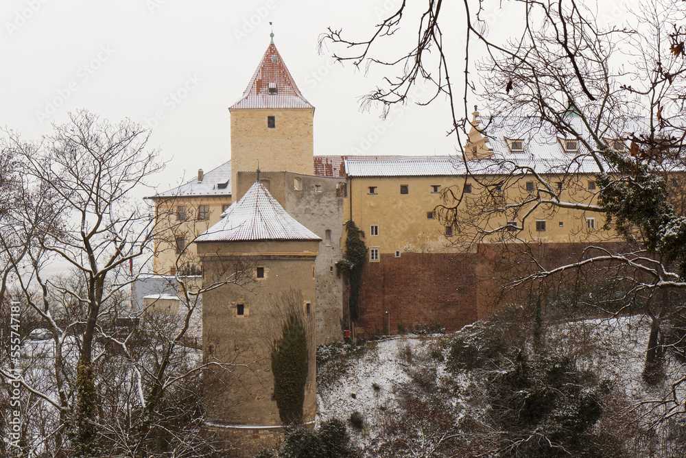 Deer Moat and Daliborka tower in foreground with snow-covered roofs of Prague Castle in winter, no people.