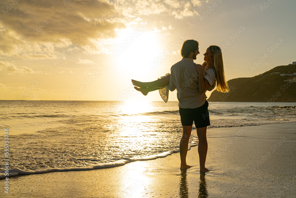Young man holding up woman on the beach during sunset as they look into each other's eyes