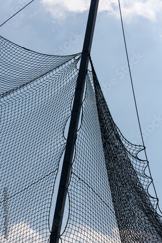 Ein grobes Netz ist an einem Pfahl gebunden vor einem blauen Himmel mit weißen Wolken.