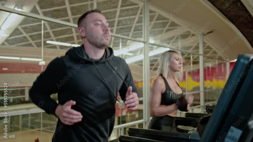 Young athletic man and woman exercising and running on treadmill in sport gym