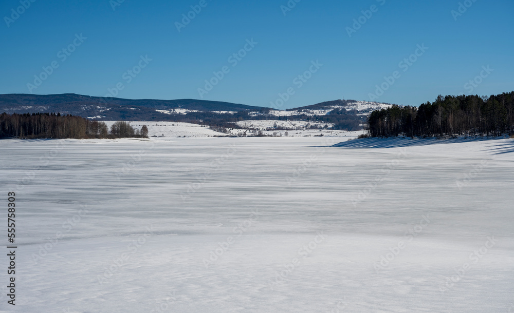 Winter landscape by the frozen lake with hills in the background background. Frozen Lake on a cold winter day