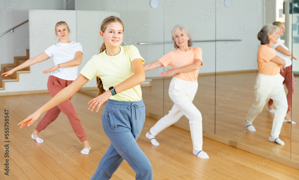 Ordinary teen girl with family exercising dance moves with group of people in dance center