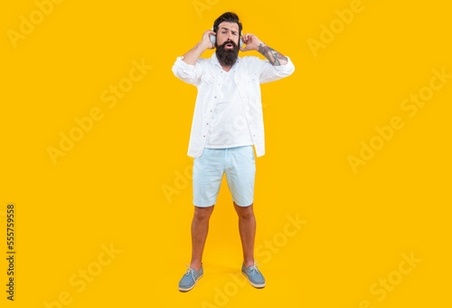 confused bearded man listening music in headphones isolated on yellow. man listening music
