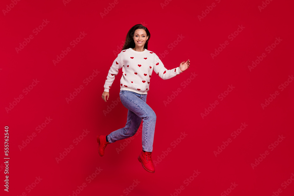 Full length photo of shiny sweet lady wear white sweater walking smiling jumping high isolated red color background