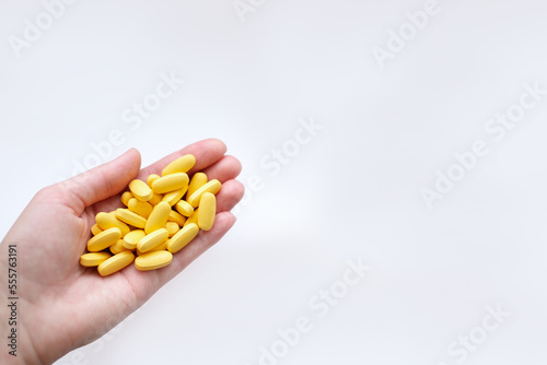 Close-up texture of yellow multivitamin tablets in female hand on white background. Healthy lifestyle concept