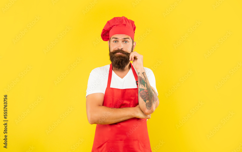 Man in red apron and toque twirling moustache with puzzled look yellow background, cook