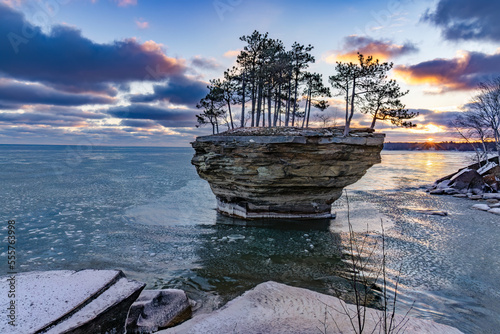 The sun begins to rise over Lake Huron and illuminate the skies and reflect off the waters surface. A rock formation known as Turnip Rock stands tall, amongst the pancake ice that's beginning to form 