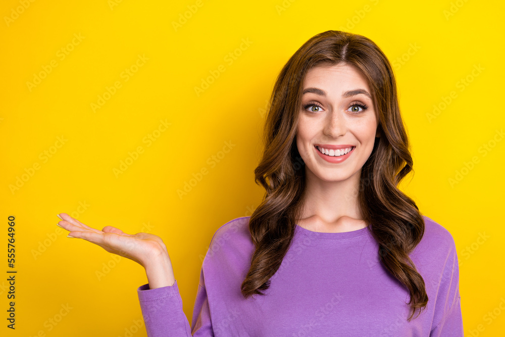 Photo of cute excited lady wear purple jumper wavy brown hair toothy beaming smile hold arm mockup promo isolated on bright yellow color background - obrazy, fototapety, plakaty 