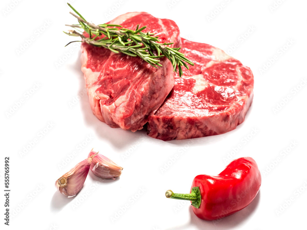 Fresh premium rib eye steak on white isolated background with green herb and garlic clove and red pepper. Premium beef cut. Top quality meat.