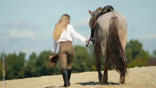 Back view of a girl strolling with a horse along the river shore. Equestrian rider walks her charming animal within sandy beach. High quality 4k footage
