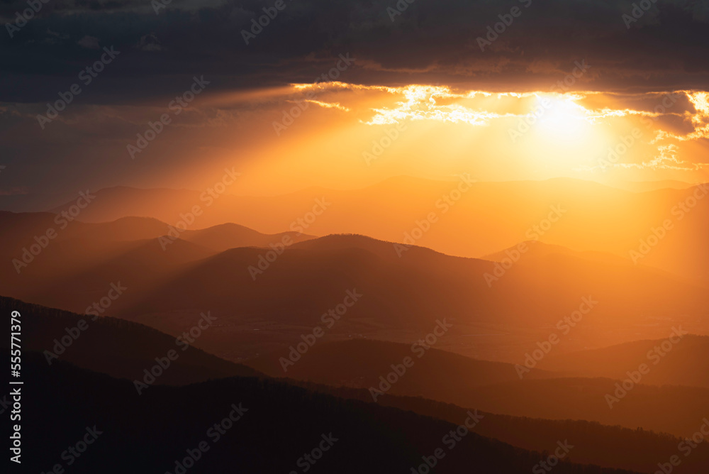 Golden crepuscular rays spill out and illuminate the mountains and valleys of Shenandoah National Park. Golden crepuscular rays spill out and illuminate the mountains and valleys of Shenandoah National Park.