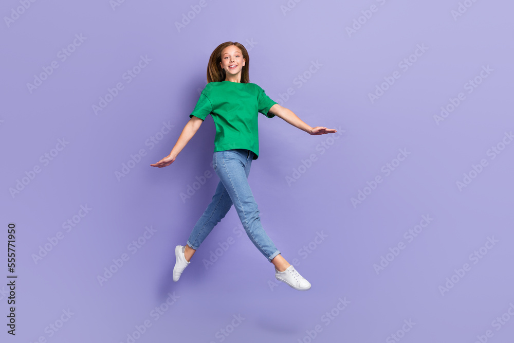 Full length photo of shiny adorable small lady wear green t-shirt jumping high walking isolated violet color background