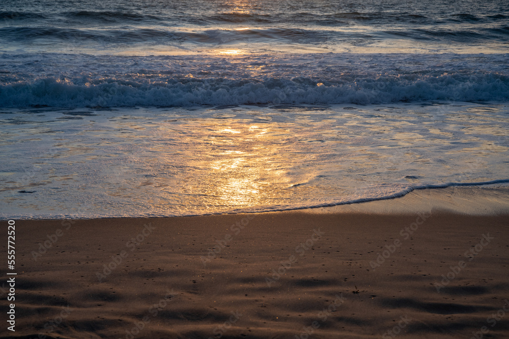 Obraz premium Sunset, sunlight reflected in the outgoing waves on the beach