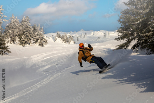 Young athletic snowboarder in bright yellow coat riding down on splitboard splashing snow