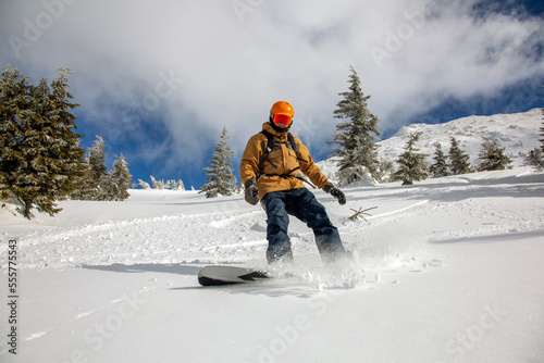 Young athletic snowboarder in bright yellow coat riding down on splitboard splashing snow