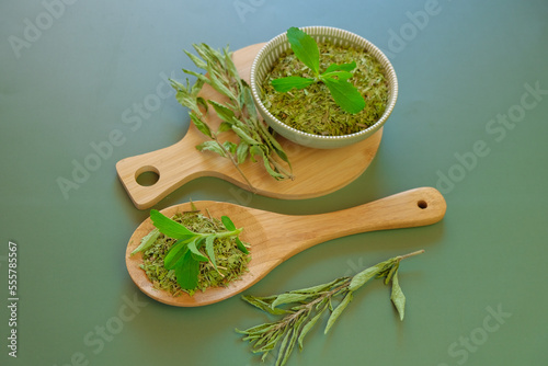 Stevia rebaudiana.Stevia plant.Alternative Low Calorie Vegetable Sweetener.Dried stevia and green twig in a round cup and a wooden spoon on a olive background.Sugar substitute. Natural dietary photo