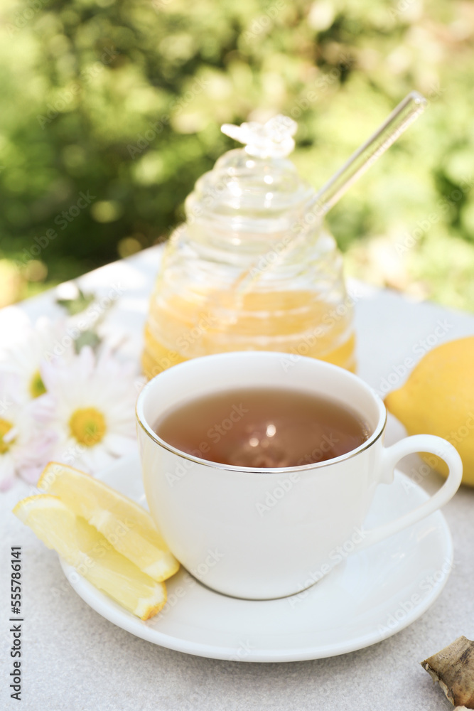 Cup of delicious tea with lemon and honey on white table outdoors