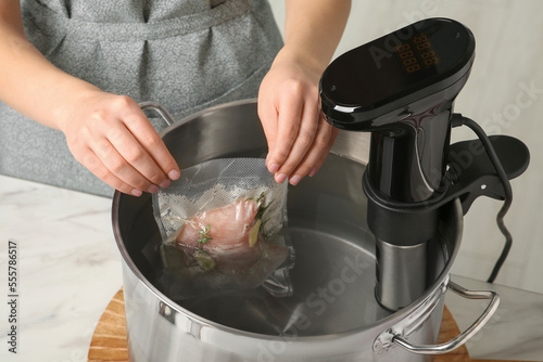 Woman putting vacuum packed meat into pot in kitchen, closeup. Thermal immersion circulator for sous vide cooking photo