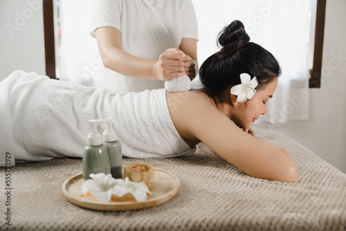 Relaxed pretty asian young woman enjoying remedial body massage done by professional masseur in spa room, with herbal compress balls in therapy spa salon.