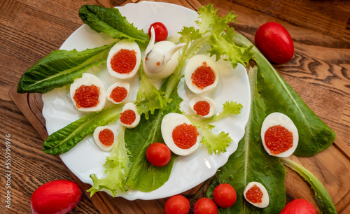 background of red caviar on dark wooden surface. edible egg rabbit figurine for decorating dishes easter dish decorated with red painted Easter eggs, cherry tomatoes and lettuce leaves