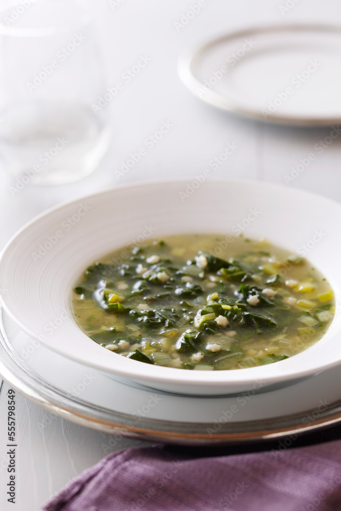 Bowl of leafy green soup with star shaped pasta on a white background with a purple napkin Bowl of leafy green soup with star shaped pasta on a white background with a purple napkin