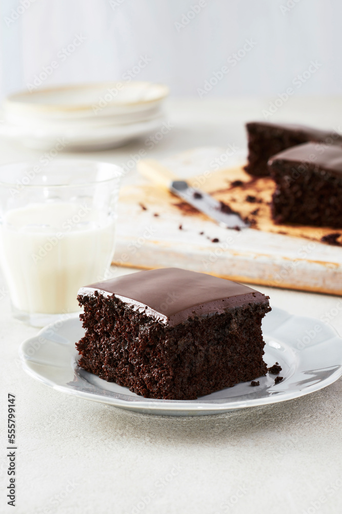 Piece of dark, chocolate cake with chocolate icing on a dessert plate with a glass of milk Piece of dark, chocolate cake with chocolate icing on a dessert plate with a glass of milk