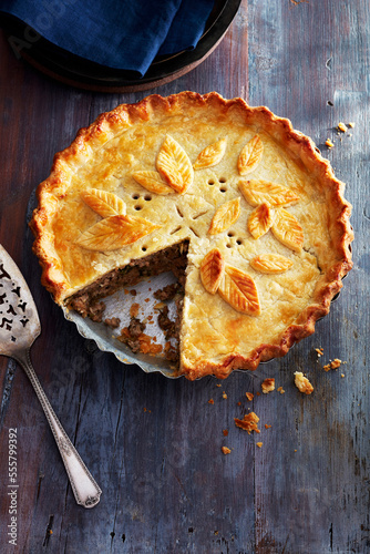 Tourtiere with a decorated crust and one piece taken out on a blue wooden background