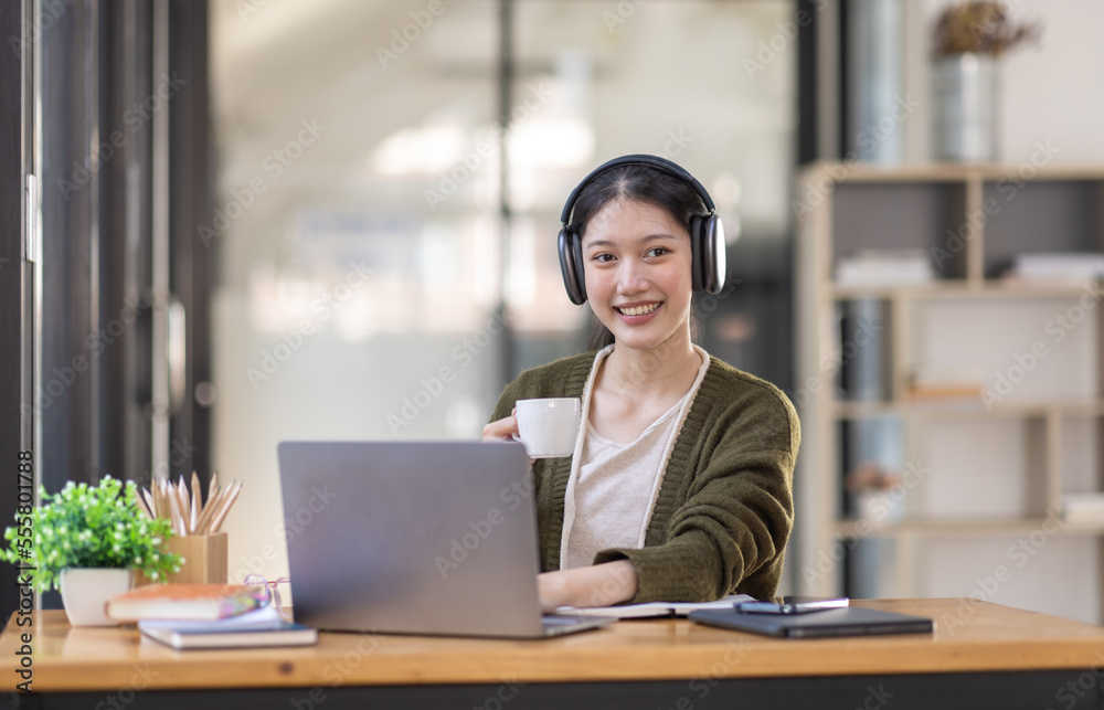 Young adult happy smiling Hispanic Asian girl student wearing headphones talking on online chat meeting using laptop in university campus or at virtual office. College female student learning remotely Young adult happy smiling Hispanic Asian girl student wearing headphones talking on online chat meeting using laptop in university campus or at virtual office. College female student learning remotely