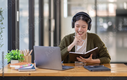 Young adult happy smiling Hispanic Asian girl student wearing headphones talking on online chat meeting using laptop in university campus or at virtual office. College female student learning remotely