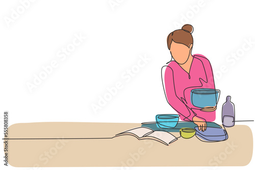 Single one line drawing beautiful woman cooking meal while reading tutorial book on cozy kitchen table at home. Healthy food lifestyle. Modern continuous line draw design graphic vector illustration