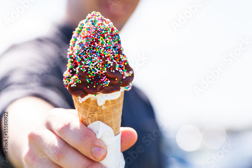 Person holding out soft serve ice cream with chocolate topping and sprinkles on summers day photo