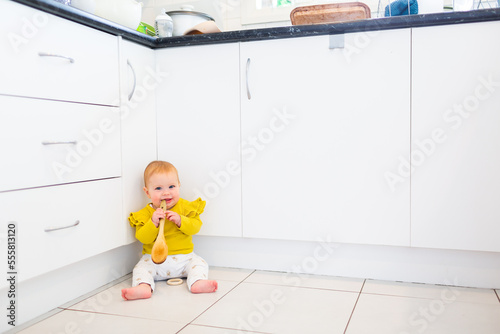 Baby sitting on flor of messy kitchen playing with wooden spoon photo
