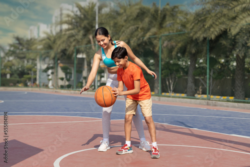 Girl and her younger brother, teenager, play basketball on modern basketball court under open sky. © G-images