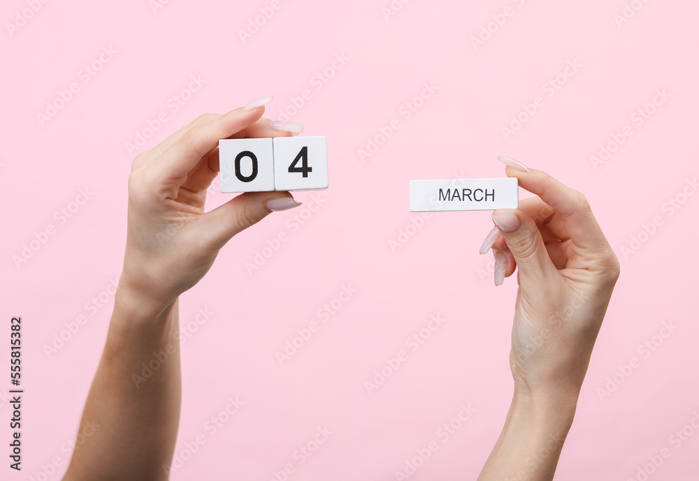 Woman's hands hold wooden block calendar with the date 04 march on pink background Woman's hands hold wooden block calendar with the date 04 march on pink background