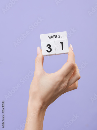 Block calendar with date march 31 in female hand on pastel color lavender background