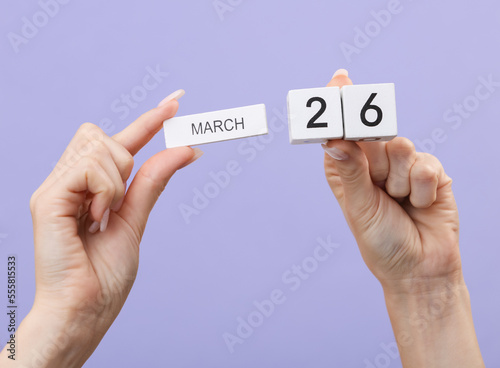 Block calendar with date march 26 in female hands on pastel color lavender background