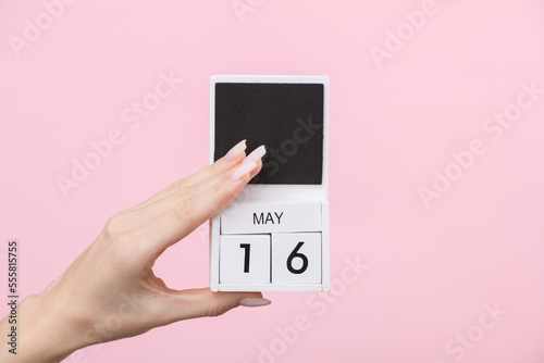 Block calendar with date may 16 in female hand on pink background