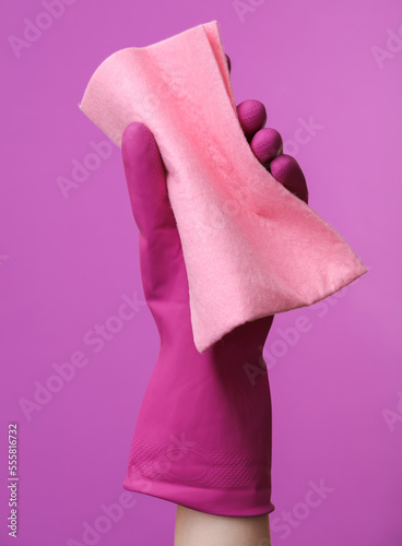 Hand in purple rubber cleaning glove holding rag on purple background. House cleaning and housekeeping concept