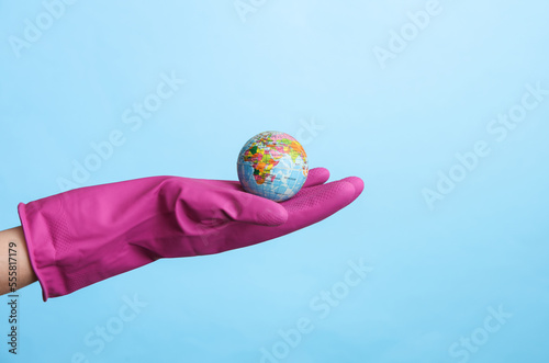 Fototapeta Naklejka Na Ścianę i Meble -  Hand in purple rubber cleaning glove holding globe on blue background. House cleaning and housekeeping concept