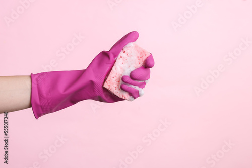 Woman's hand in glove holds sponge in foam on a pink background. Cleaning concept