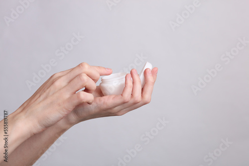 Woman's hands holding white jar of cream on gray background