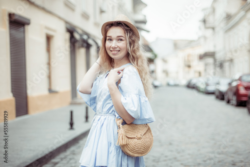 Cute young woman in a hat and dress has fun on European street