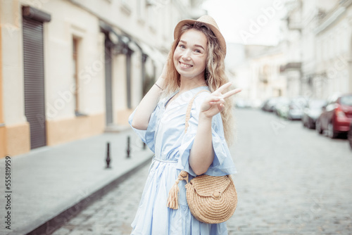 Cute young woman in a hat and dress has fun on European street